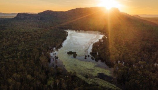 Aerial photo of a river with the sun setting behind some mountains